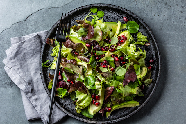 lettuce salad with pomegranate on black plate. top view