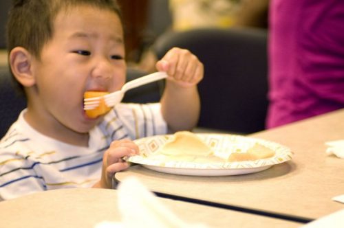 child holding a plastic fork in his right hand with which hed speared a piece of cantaloupe 725x482